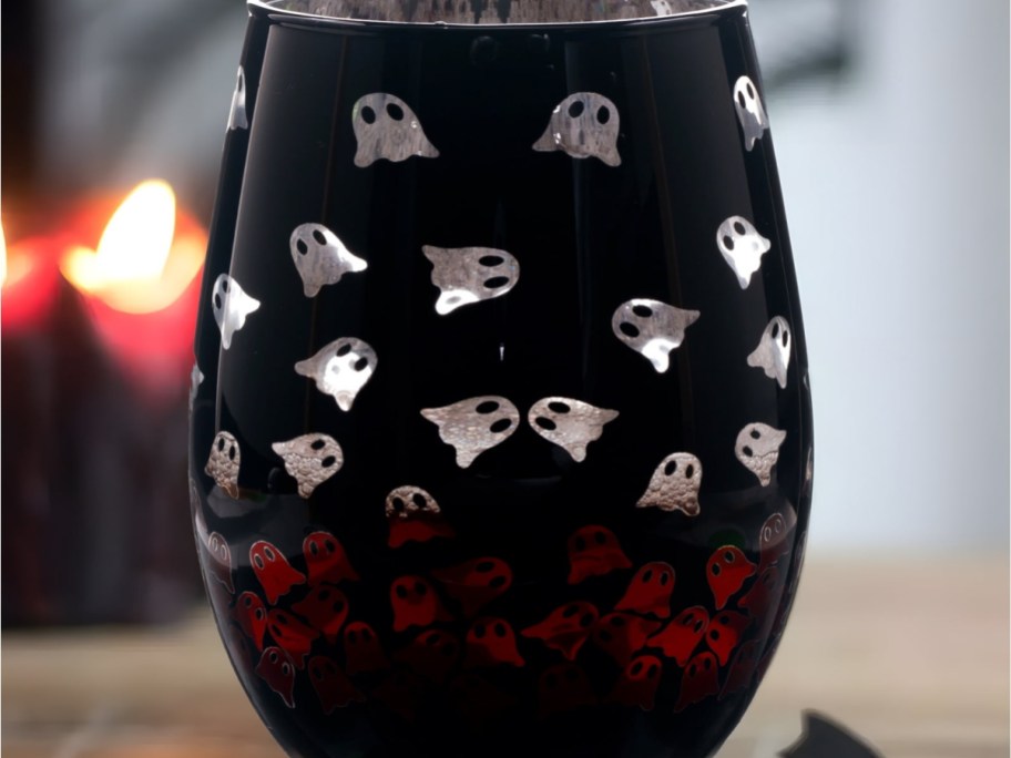 A dark stemless glass decorated with a pattern of small silver ghosts across the top and red ghosts clustered near the bottom.