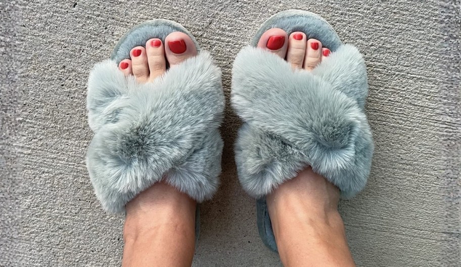 a womans feet with red toe nails wearing a pair of faux fur crossband house slippers