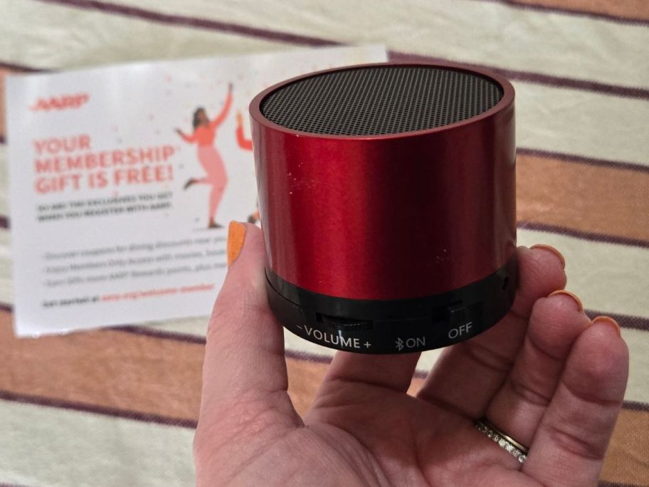 Hand holding a free red mini wireless speaker from AARP