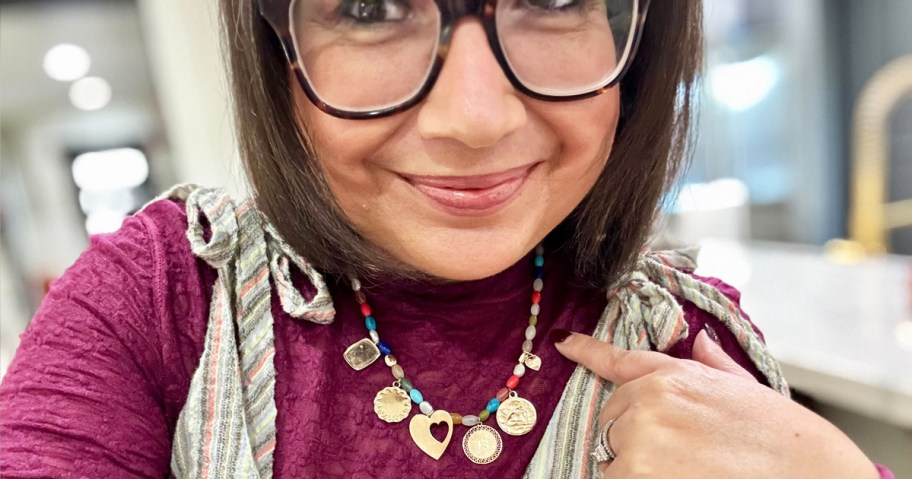 woman wearing and pointing to a beaded charm necklace