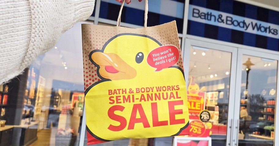 woman holding up a Bath & Body Works Semi-Annual Sale outside of store