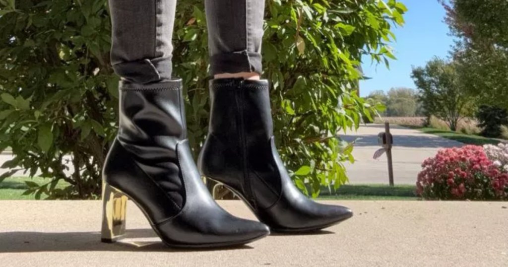 Woman wearing short, black leather boots with gold colored heel and standing outside