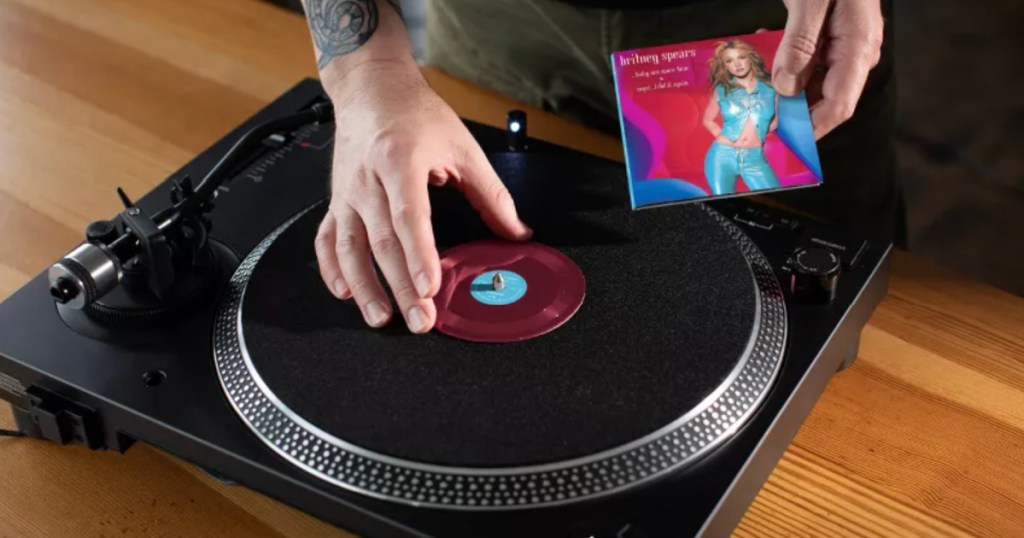 Man putting tiny record with Britney Spears music onto record player