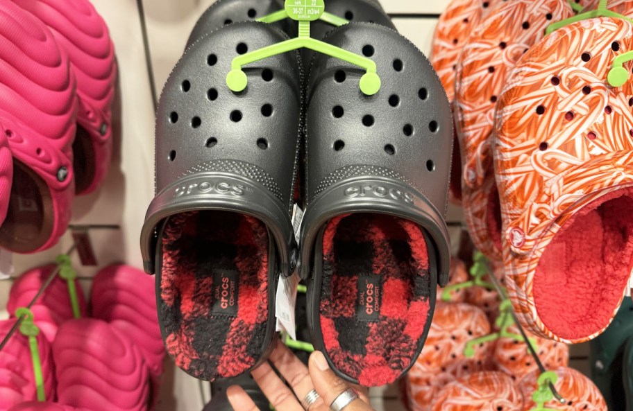 hand touching a pair of black crocs with red buffalo check fuzzy lining