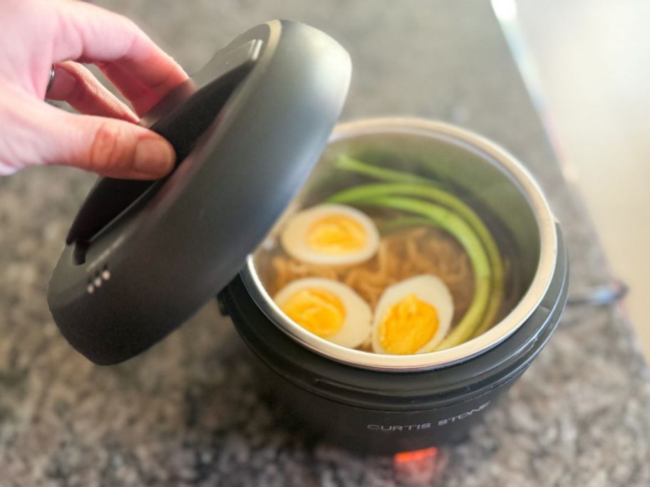 Hand holding the lid on a Curtis Stone portable food warmer with ramen inside
