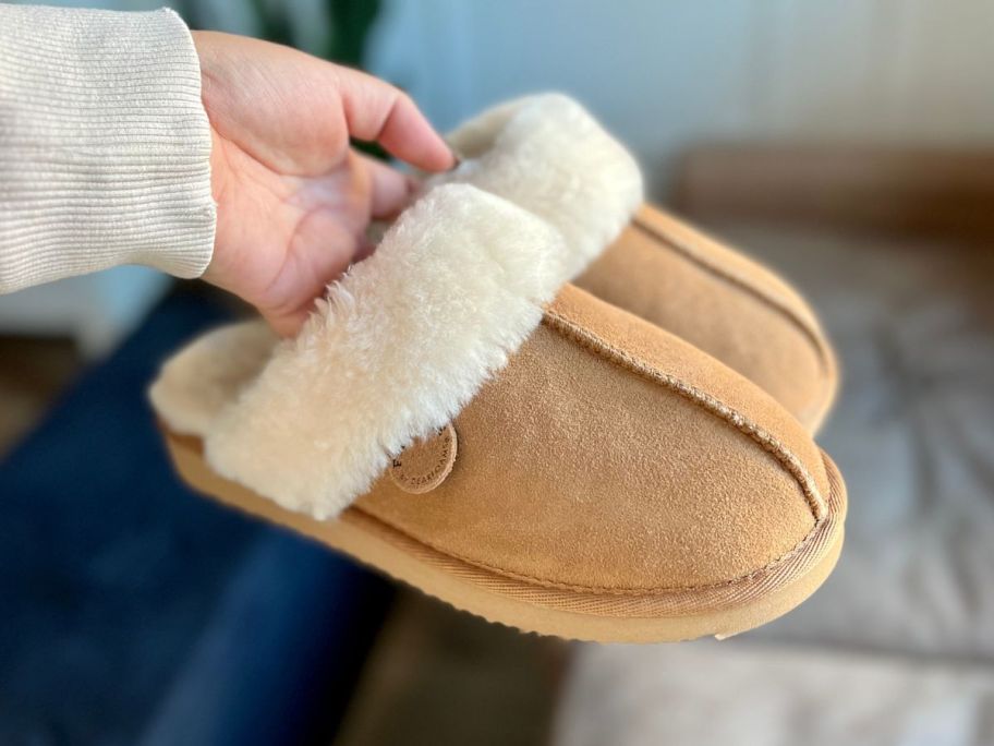 Hand holding a pair of dearfoams fireside scuff slippers