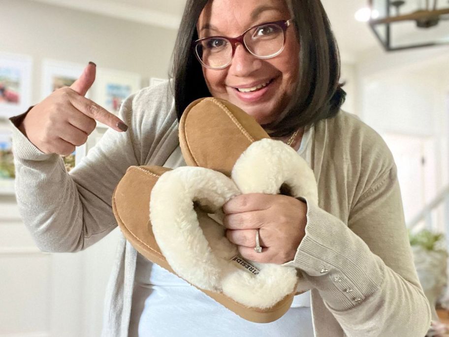 Woman holding a pair of dearfoams Fireside slippers
