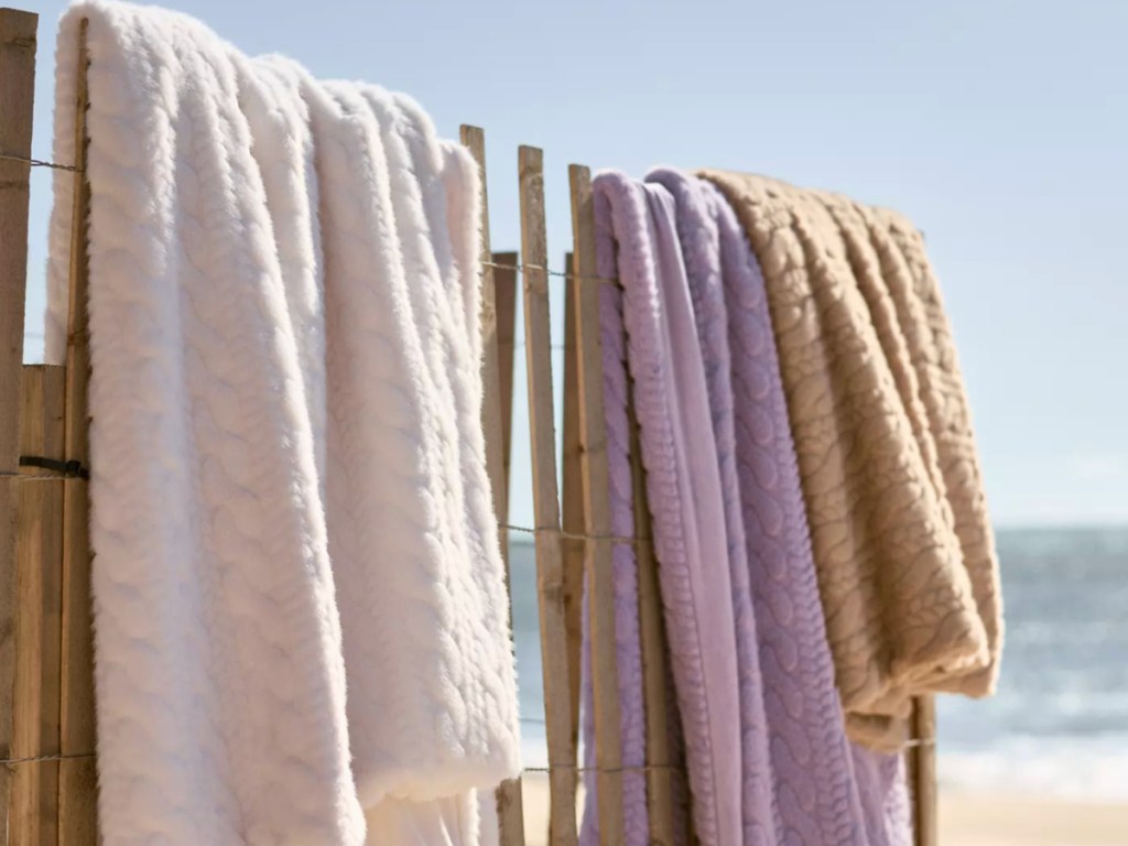 Faux Fur Cable-Knit Sweater Throw Blankets draped over fence on beach