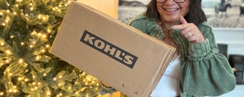 woman standing by a Christmas tree holding and pointing to a Kohl's box