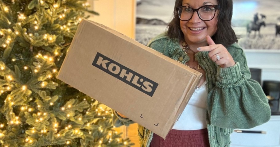 woman standing by a Christmas tree holding and pointing to a Kohl's box