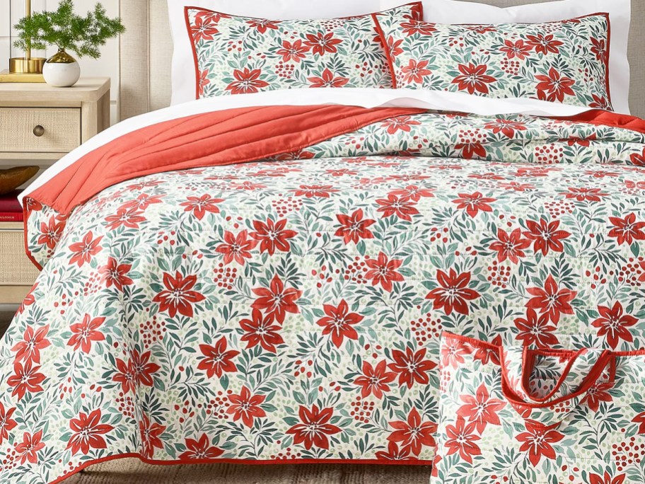 Poinsettia print quilt and shams set on a bed with a matching tote bag