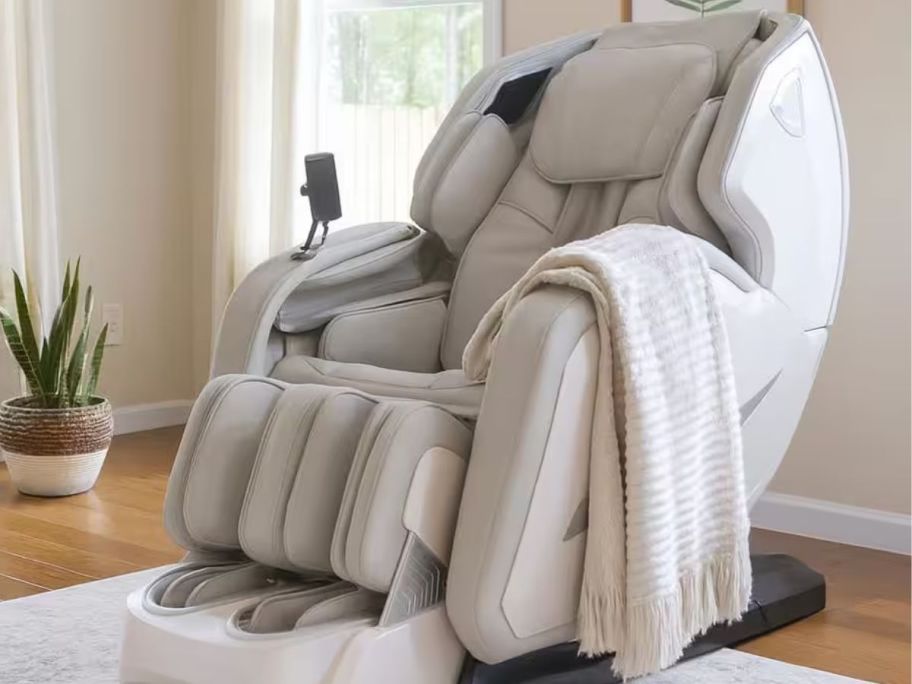 A taupe faux leather massage chair in a living room with a throw blanket on the arm