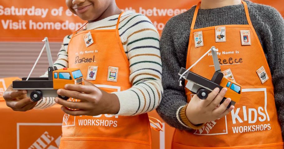 2 kids in orange Home Depot aprons, holding tow trucks that they presumably built