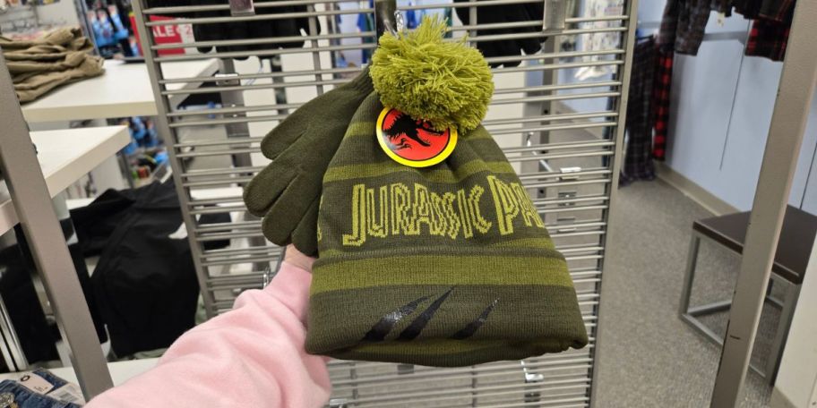 A person holding a green Jurassic Park hat and glove set