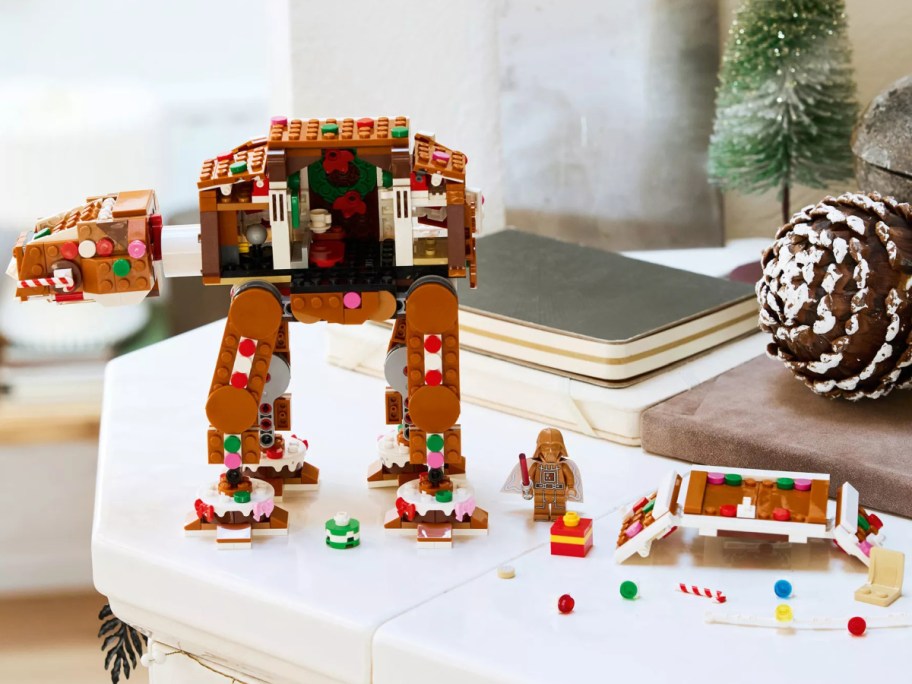 A gingerbread-themed LEGO Star Wars AT-AT Walker decorated with colorful candy pieces and white frosting, standing next to a gingerbread Darth Vader minifigure.