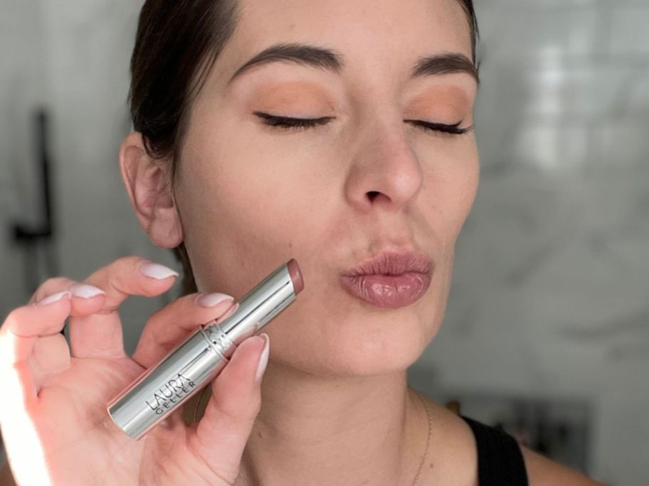 Woman holding a tube of Laura Geller Jelly Balm next to her puckered lips
