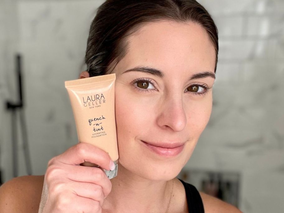 Woman holding a Laura Geller Quench & Tint Foundation next to her face