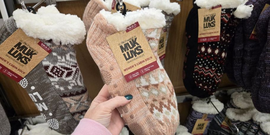 a person touching a pink Muk Luk sock slipper