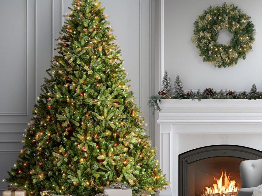 A lit Christmas tree in a living room next to a fireplace.