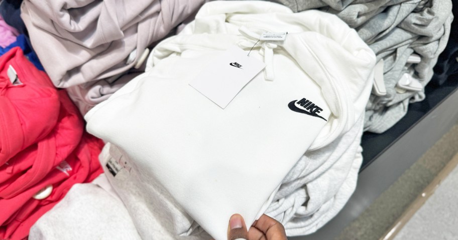 hand touching a white folded nike hoodie on store display table