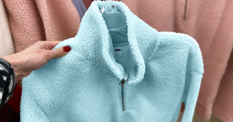 hand holding up a blue sherpa jacket on a hanger in store