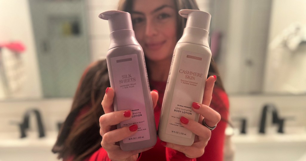 Woman holding up two bottles of scent theory lotions while standing in bathroom