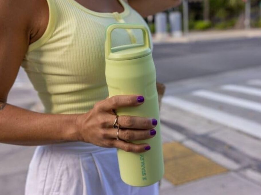 A woman in a green tank top holding a green Stanley water bottle