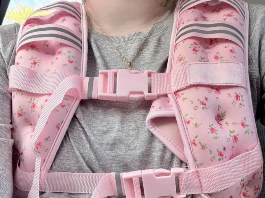 Pink floral weighted vest strapped on a woman with a gray shirt