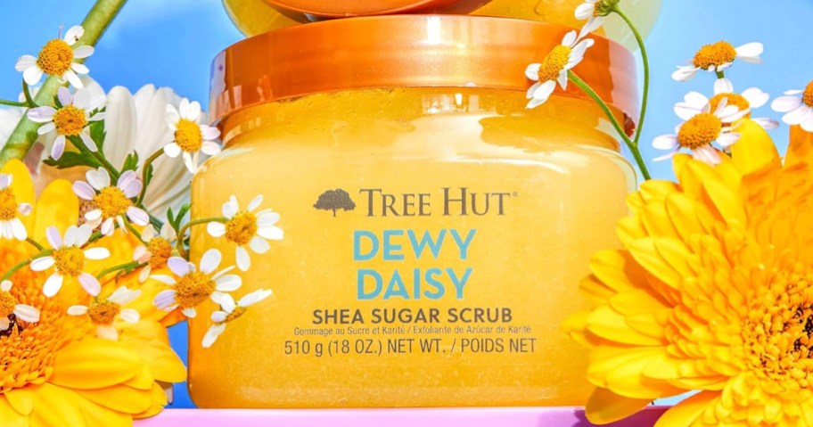 yellow jar of tree hut sugar scrub near yellow flowers