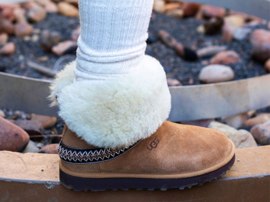 A person wearing a boot with fur near a fire pit 