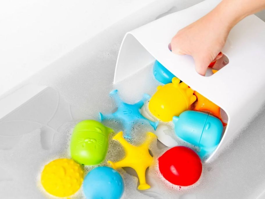 A person holding a white plastic bin scooping up colorful bath toys in the bath