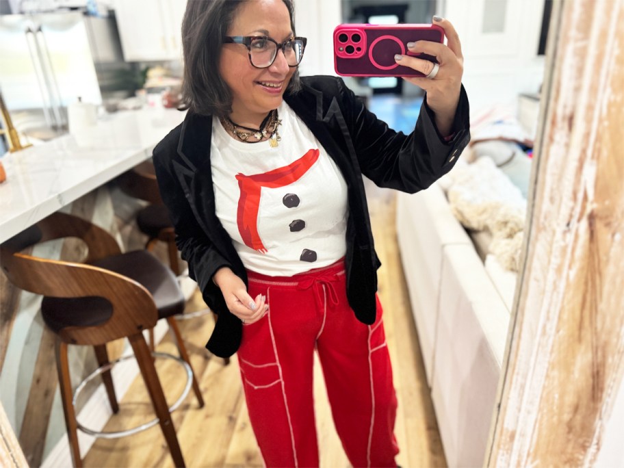 woman taking photo in mirror wearing a snowman shirt with red pants