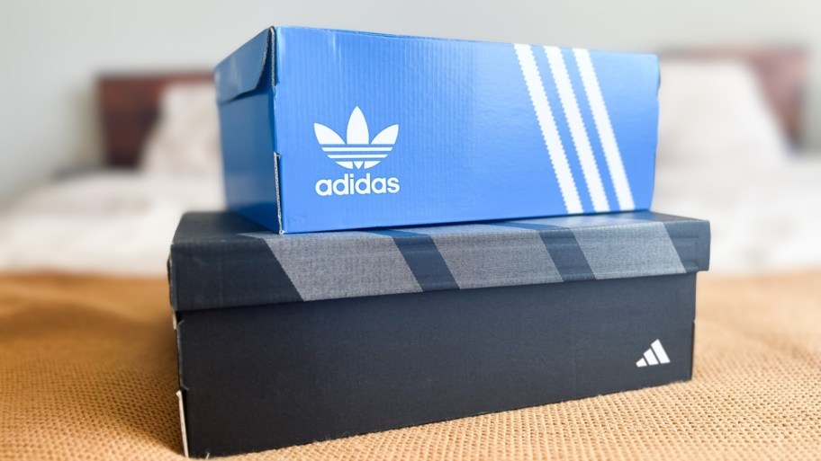 two adidas shoes boxes on the foot of a bed