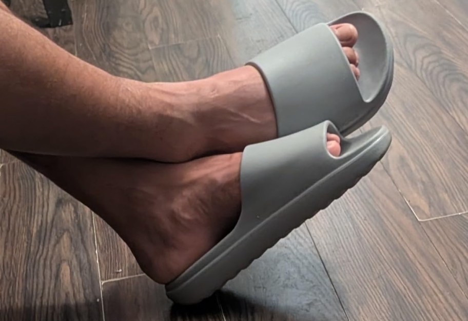 feet wearing gray slides on wood floor