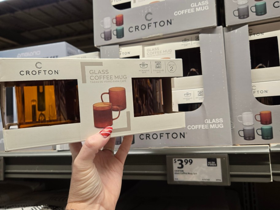 A hand holding up a box of glass amber colored mugs at Aldi.