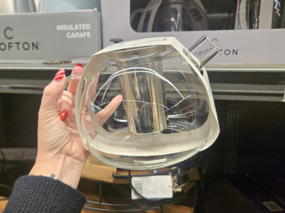 A hand hodling up a glass teapot at Aldi.