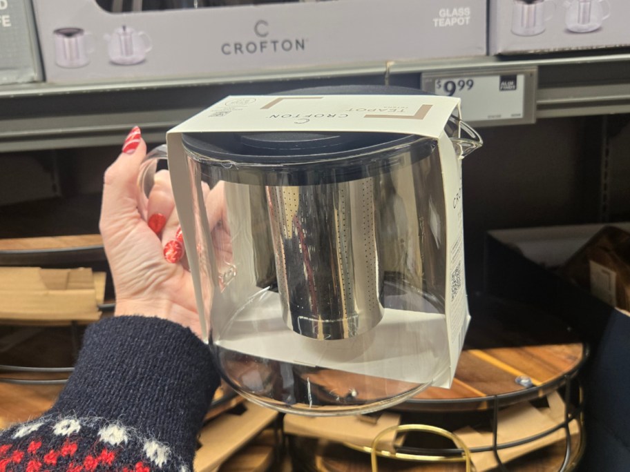 A hand hodling up a glass teapot at Aldi.