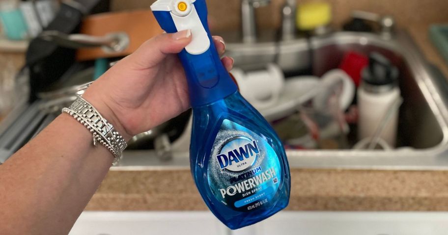 hand holding dawn powerwash spray bottle in fromt of sink with dishes in it
