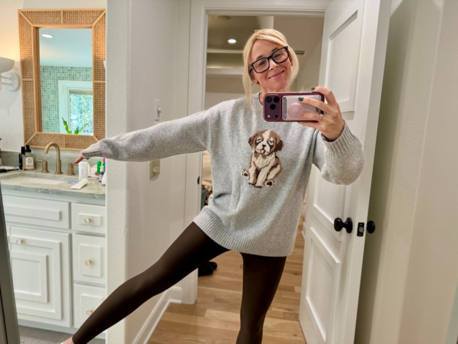 smiling woman in a dog print sweater holding a phone taking a mirror selfie