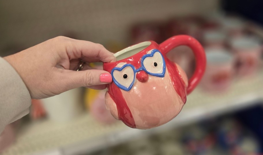 womans hand holding a coffee mug with a featherly ird painted on