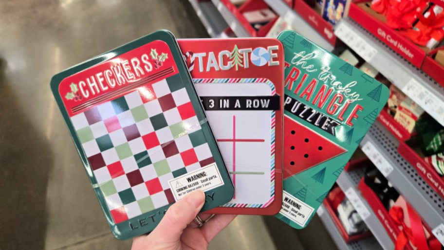hand holding three gift card game tins in a store aisle