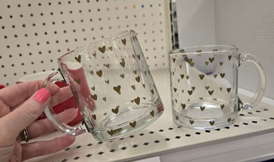 womans hand holding a glass coffee mug with gold heart print