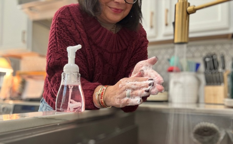 woman washing her hands at a kitchen sink, with soap next to her