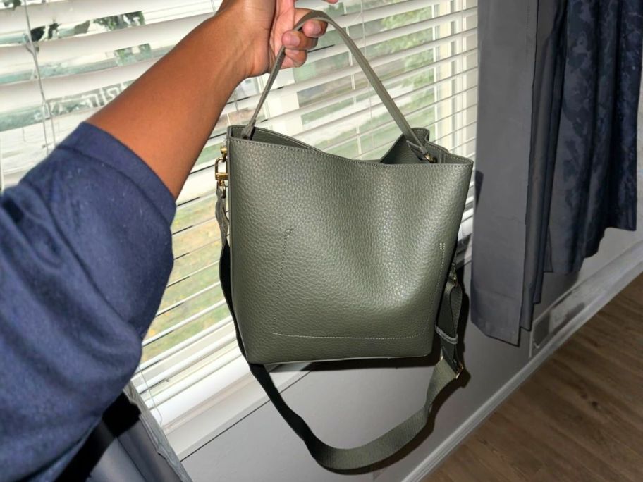 hand holding bucket bag in front of window