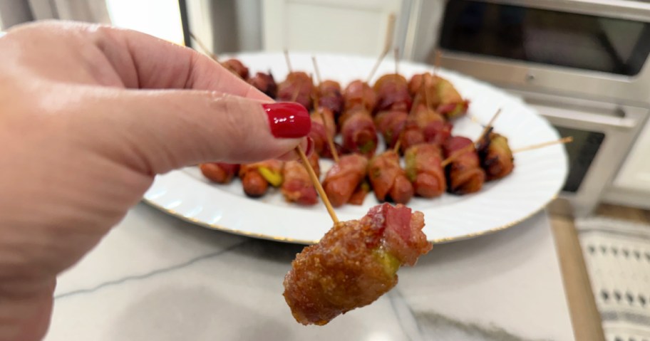 holding a bacon wrapped sausage on a toothpick