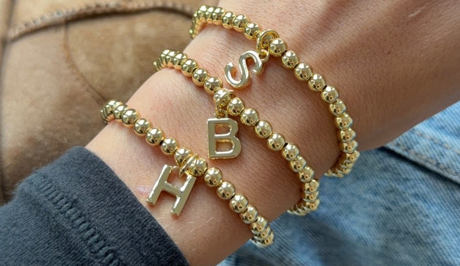a womans wrist wearing a stack of initial bracelets