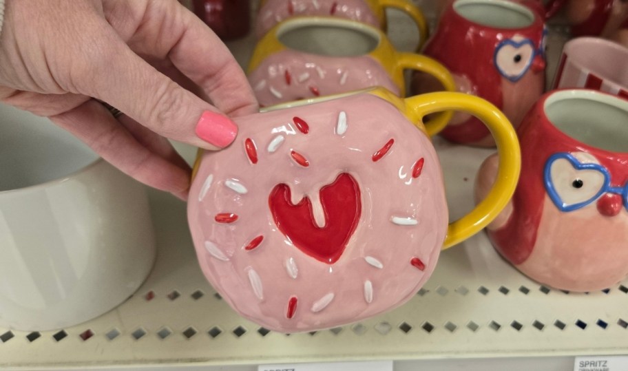 womans hand holding a pink donut coffee mug