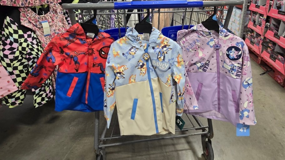 3 kids rain jackets hanging on a shopping cart