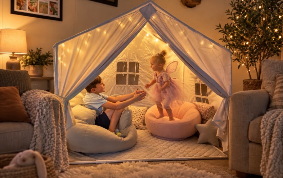 Play tent with two kids and string lights playing inside on pillows