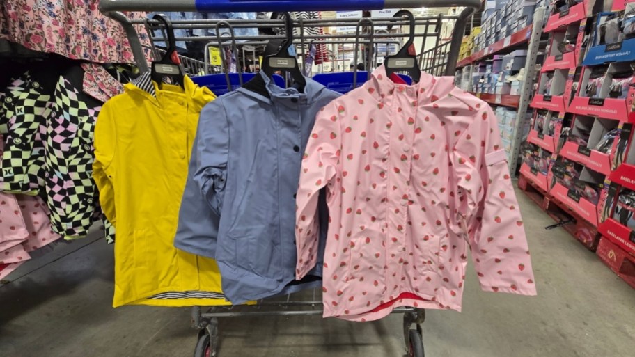 3 kids rain jackets hanging on a shopping cart